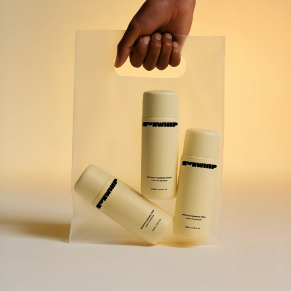 Three skincare bottles on a clear stand with a hand holding the stand against a warm background